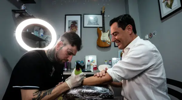 Un hombre sonriente recibe un tatuaje de un artista con estilo, considerado el mejor tatuador del mundo.