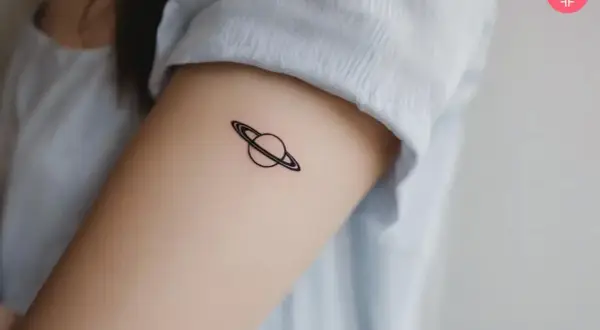 Tatuaje minimalista de Saturno en el brazo. Tatuarse Saturno puede simbolizar madurez, responsabilidad y el paso del tiempo.