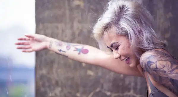 Mujer sonríe bajo la lluvia, con su brazo lleno de tatuajes, recordando el día que decidió hacerse un tatuaje.