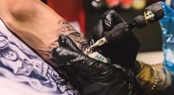 Manos enguantadas crean arte en la piel, un detalle de la **convención tatuajes**.