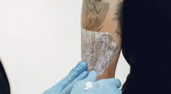Manos enguantadas aplican Bepanthol sobre un tatuaje para ayudar a su curación.