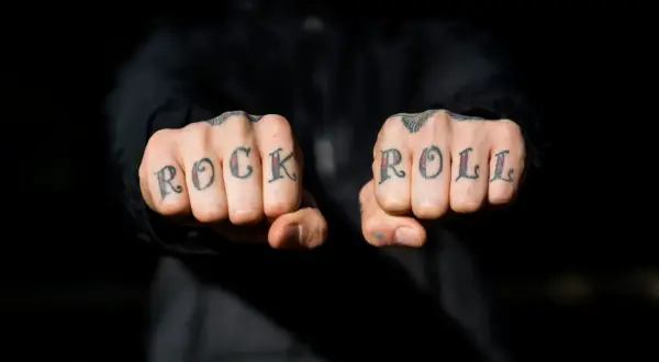 Manos con tatuajes en los nudillos que dicen "ROCK ROLL". A pesar de la pena y el pánico, el rock and roll vive.