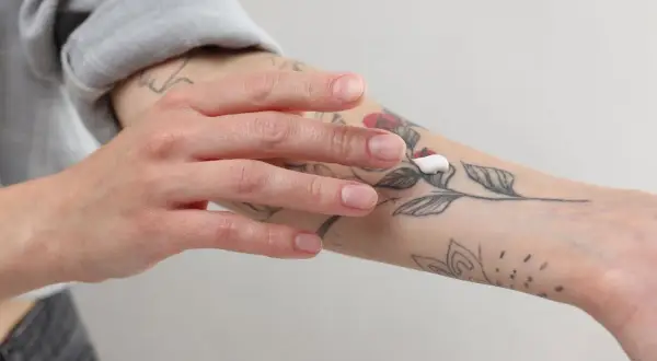 Mano aplicando crema sobre un tatuaje de flores en el antebrazo.