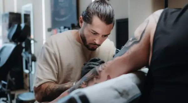 Toni Nova, un artista del tatuaje, trabaja con concentración en el brazo de un cliente.