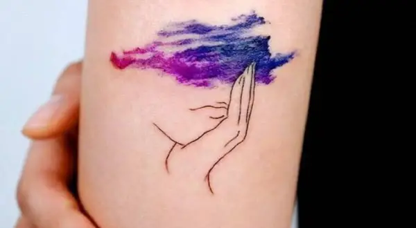 Tatuaje de una mano sosteniendo una nube morada y azul, simbolizando la superación de la ansiedad.