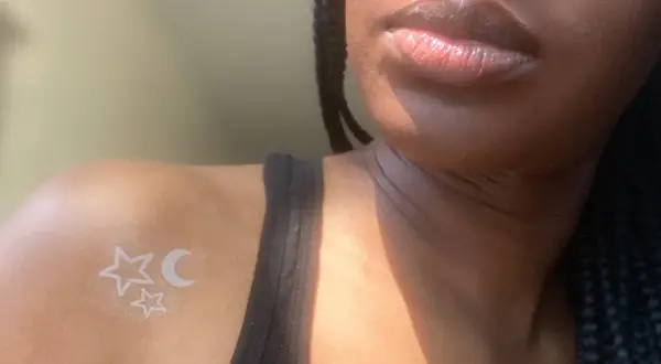 Un delicado tatuaje de tinta blanca con estrellas y luna sobre piel negra, un toque celestial sutil.