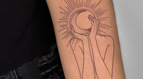 Un tatuaje de una figura abstracta abraza una luna creciente, rodeada por rayos solares. Un diseño minimalista que evoca misterio y conexión cósmica.