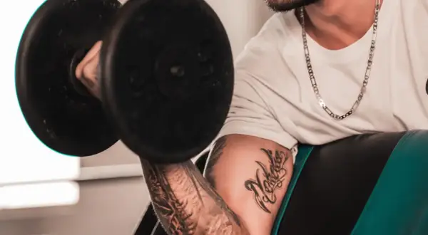 Hombre con tatuaje levanta pesa, mostrando su dedicación al deporte y su arte corporal.