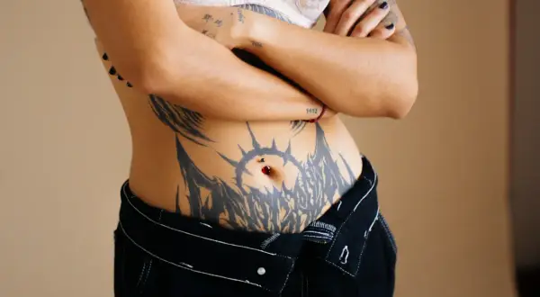 Mujer con un gran tatuaje tribal que rodea su ombligo, adornado con un piercing.