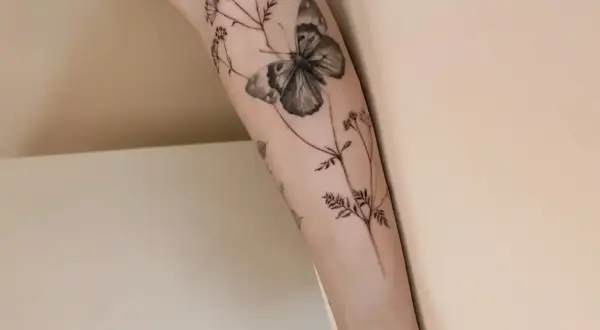 Un delicado tatuaje de mariposa y flores silvestres en un brazo, simbolizando la libertad y la belleza efímera.