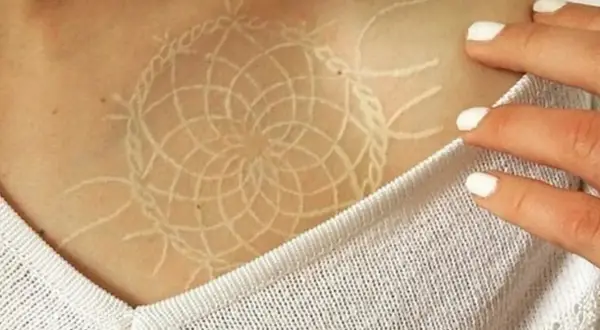 Un delicado tatuaje white out con diseño de atrapasueños en la clavícula.