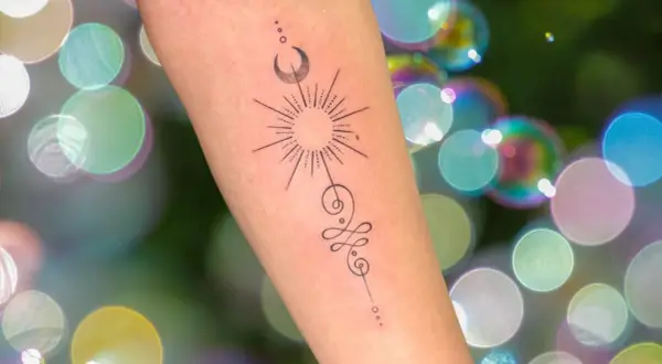 Brazo con tatuaje de sol, luna y símbolo unamalo, representando protección y tatuajes espirituales.