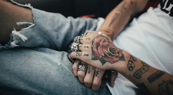 Manos entrelazadas con tatuajes de rosa y números. Reflexionando sobre a qué edad me puedo tatuar en España.