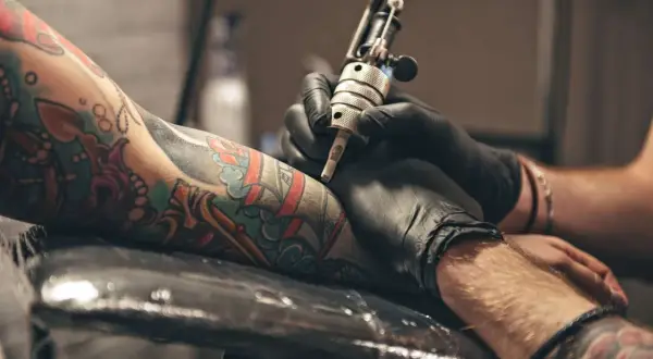 Primer plano de un brazo con tatuajes coloridos siendo tatuado por una máquina.