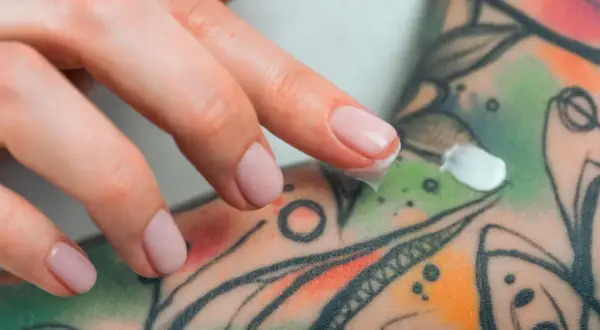 Dedos aplicando crema sobre un tatuaje colorido, parte de un proceso de cuidado y tatuaje terapéutico.