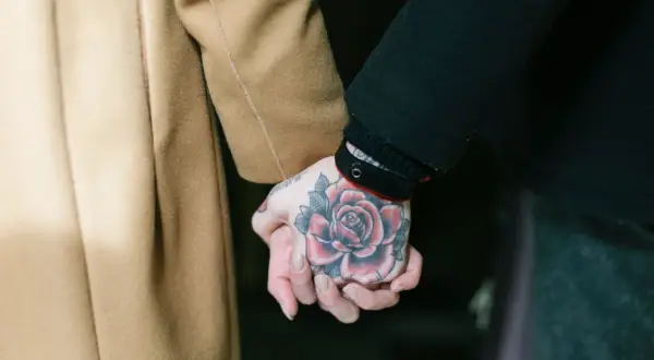 Manos entrelazadas, una con un tatuaje de rosa roja, mostrando el arte de los tatouages homme.