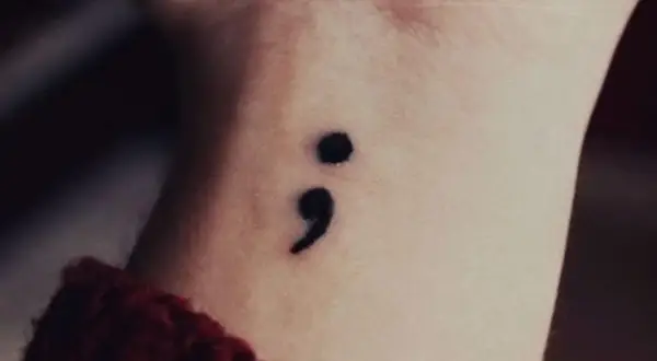 Un delicado tatuaje de punto y coma en la muñeca, símbolo de esperanza y resiliencia.