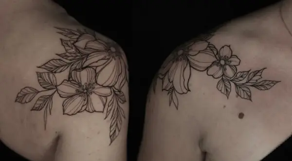 Delicados blackwork tattoos de flores y hojas adornan los hombros, creando un diseño botánico elegante y atemporal.