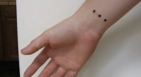Muñeca con un discreto tatuaje de tres puntos negros alineados.