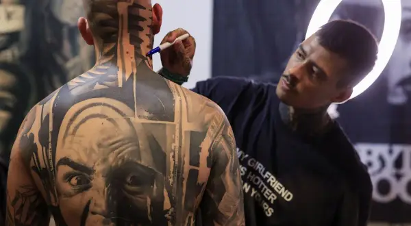 Artista de **val tattoo** retocando un intrincado diseño en la nuca de un hombre.