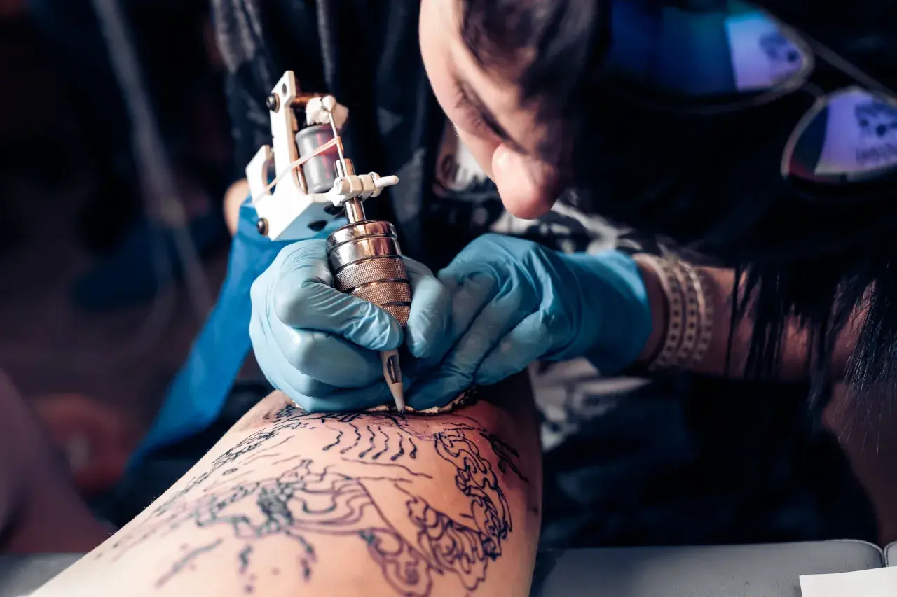 Artista tatuando en la convención de tatuajes Valencia. Manos enguantadas trabajan con precisión sobre un diseño en la piel.