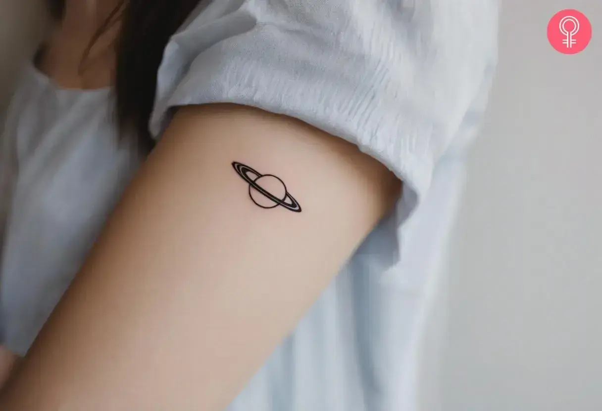 Tatuaje minimalista de Saturno en el brazo. Tatuarse Saturno puede simbolizar madurez, responsabilidad y el paso del tiempo.