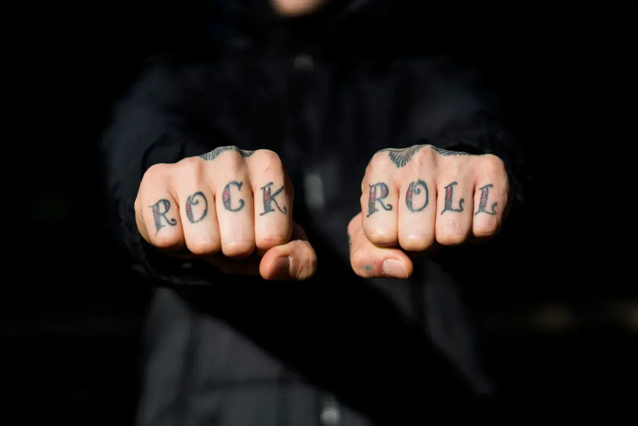 Manos con tatuajes en los nudillos que dicen "ROCK ROLL". A pesar de la pena y el pánico, el rock and roll vive.