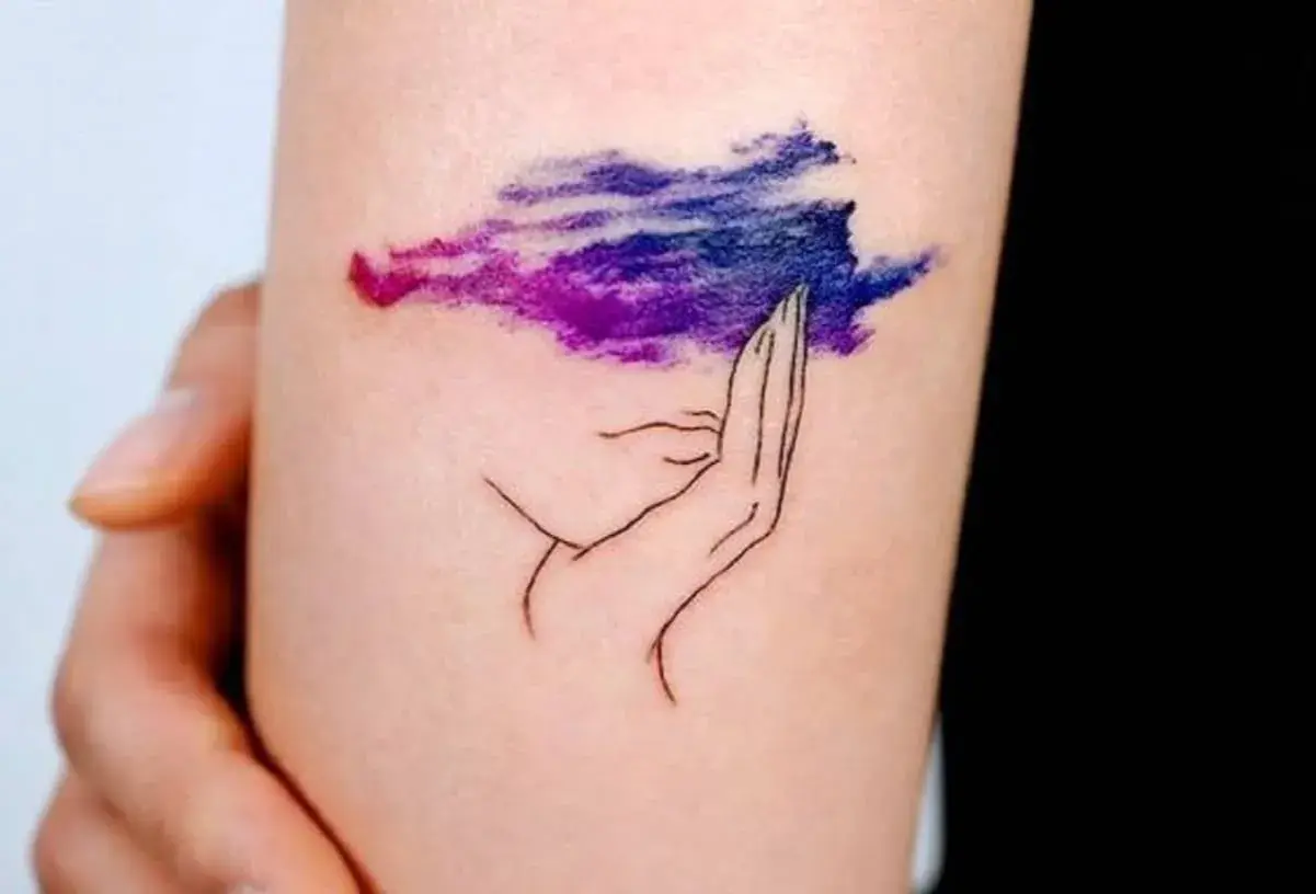 Tatuaje de una mano sosteniendo una nube morada y azul, simbolizando la superación de la ansiedad.