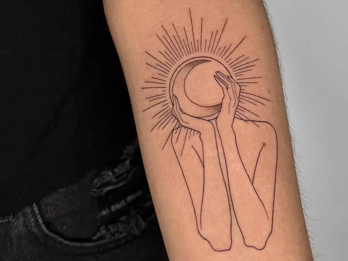 Un tatuaje de una figura abstracta abraza una luna creciente, rodeada por rayos solares. Un diseño minimalista que evoca misterio y conexión cósmica.