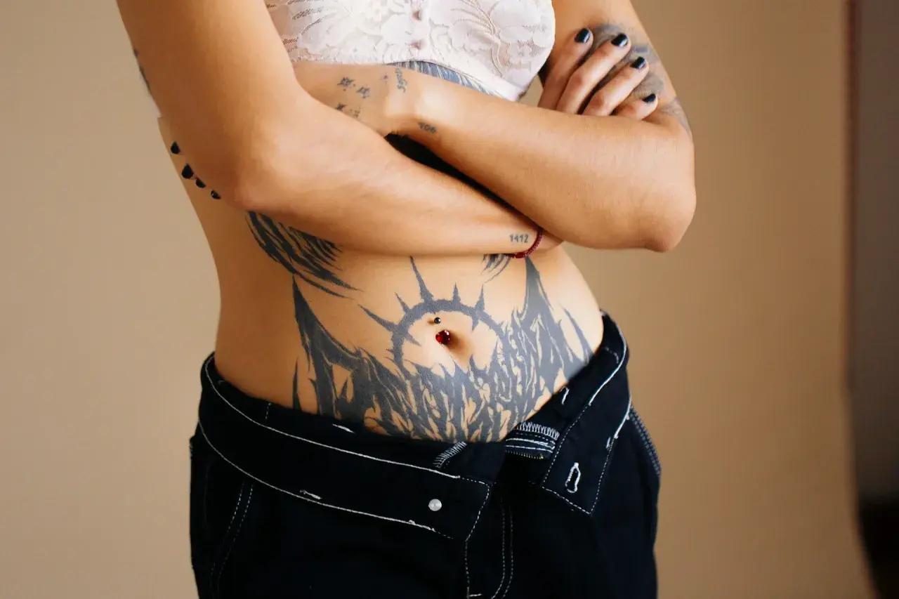 Mujer con un gran tatuaje tribal que rodea su ombligo, adornado con un piercing.