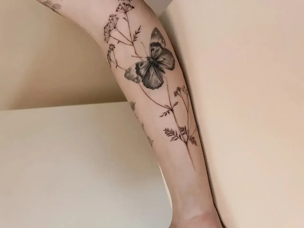 Un delicado tatuaje de mariposa y flores silvestres en un brazo, simbolizando la libertad y la belleza efímera.