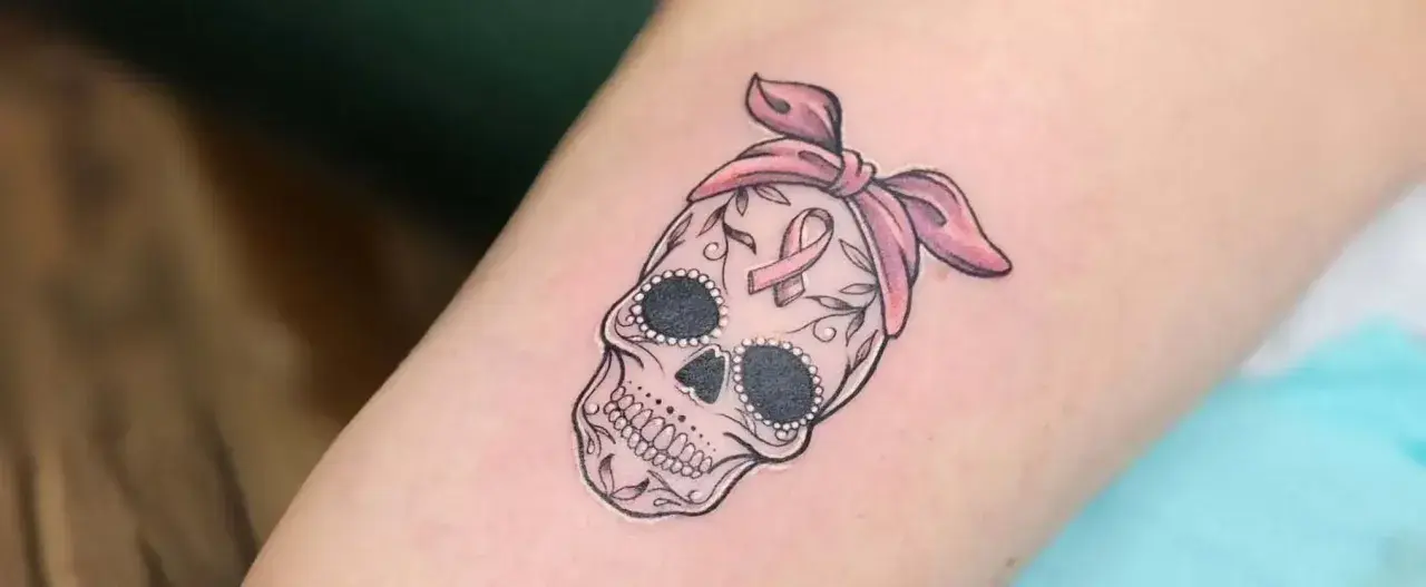 Calavera adornada con lazo rosa y cinta de concienciación, símbolo de tatuajes de superación cáncer.
