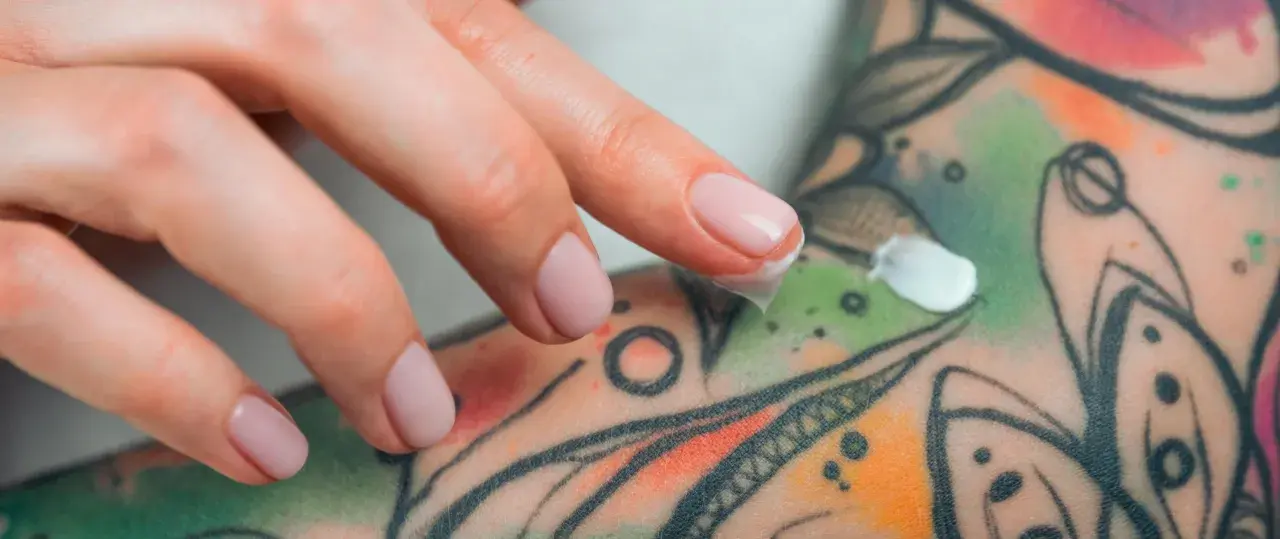 Dedos aplicando crema sobre un tatuaje colorido, parte de un proceso de cuidado y tatuaje terapéutico.