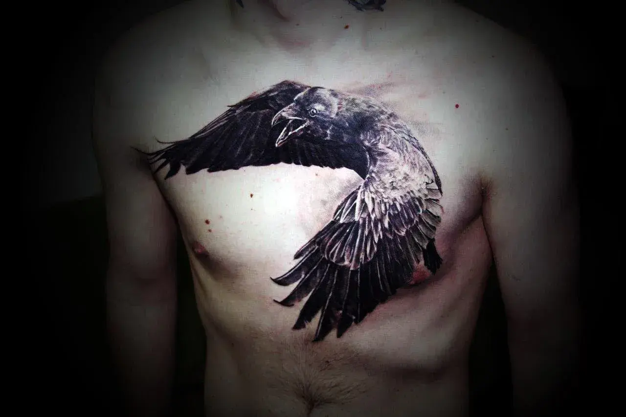 Impresionante tatuaje de cuervos en el pecho, con un ave en pleno vuelo, alas extendidas y pico abierto.