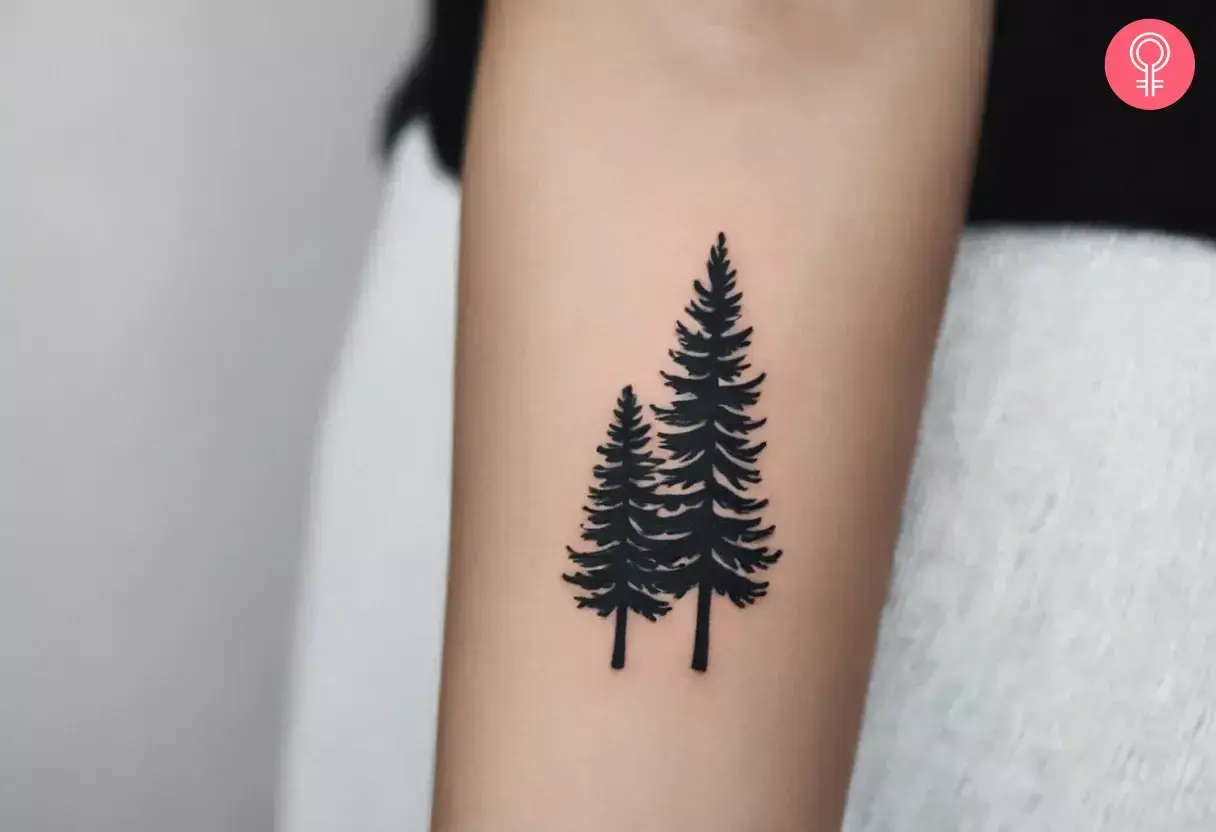 Tatuaje de dos pinos negros en un brazo, simbolizando la fuerza y el crecimiento del bosque.