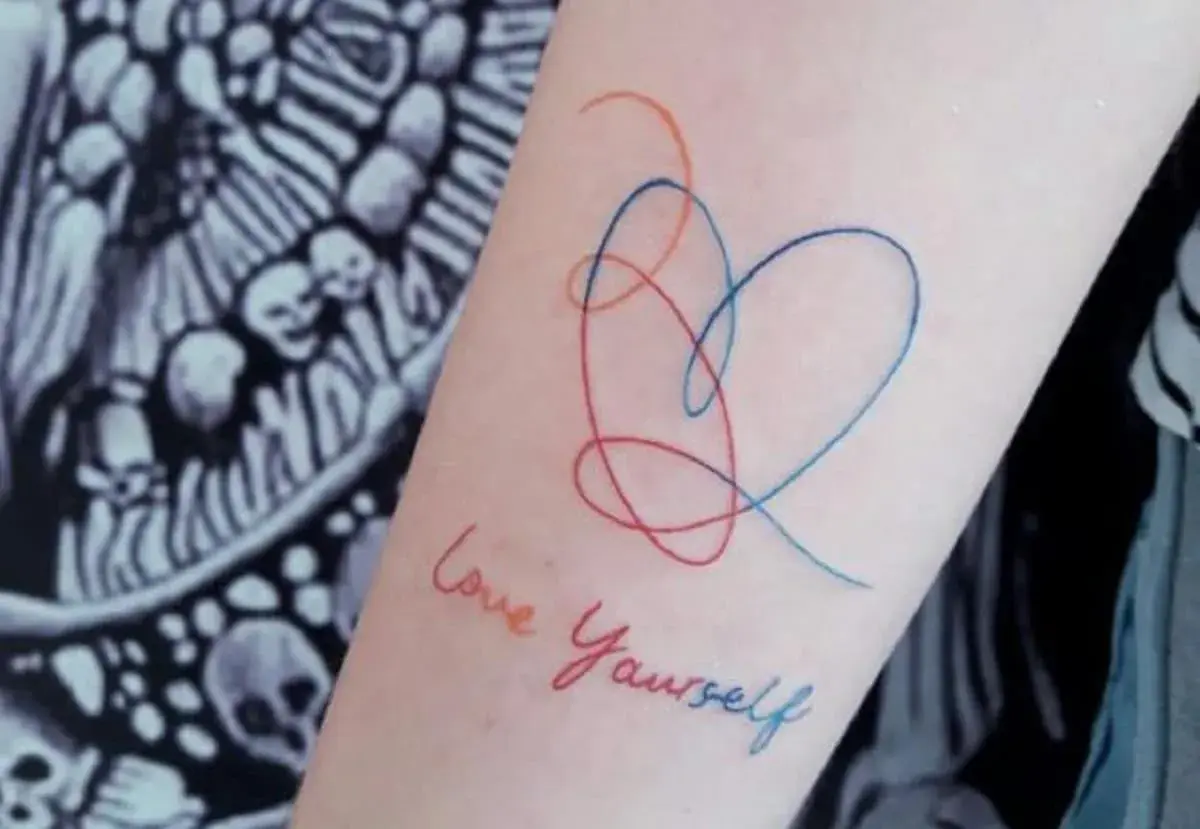 Tatuajes de corazón y "Love Yourself" en el brazo, un símbolo de fortaleza y amor propio.