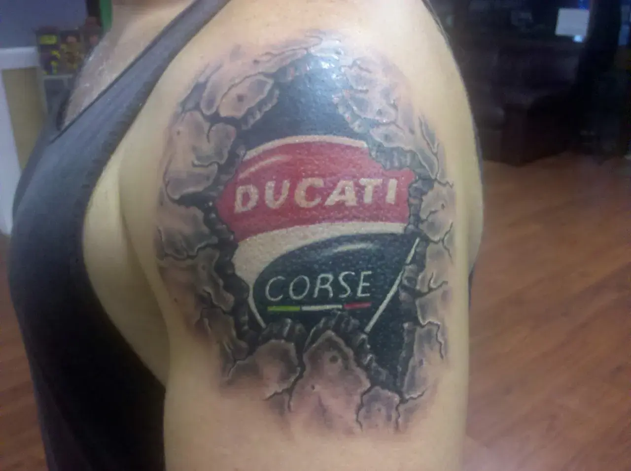 Tatuaje de un logo de Ducati Corse en el hombro, con efecto de piel rasgada.
