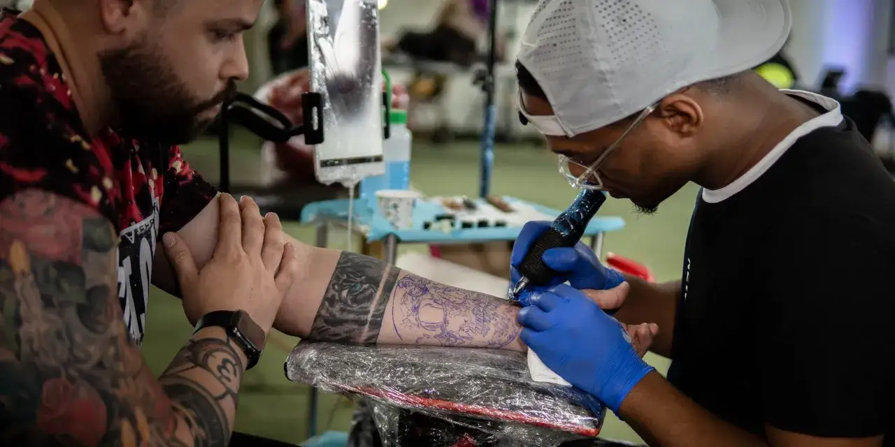 Artista de tatuajes trabajando en una convenci&oacute;n de tatuajes, creando un dise&ntilde;o detallado en el brazo de un cliente.