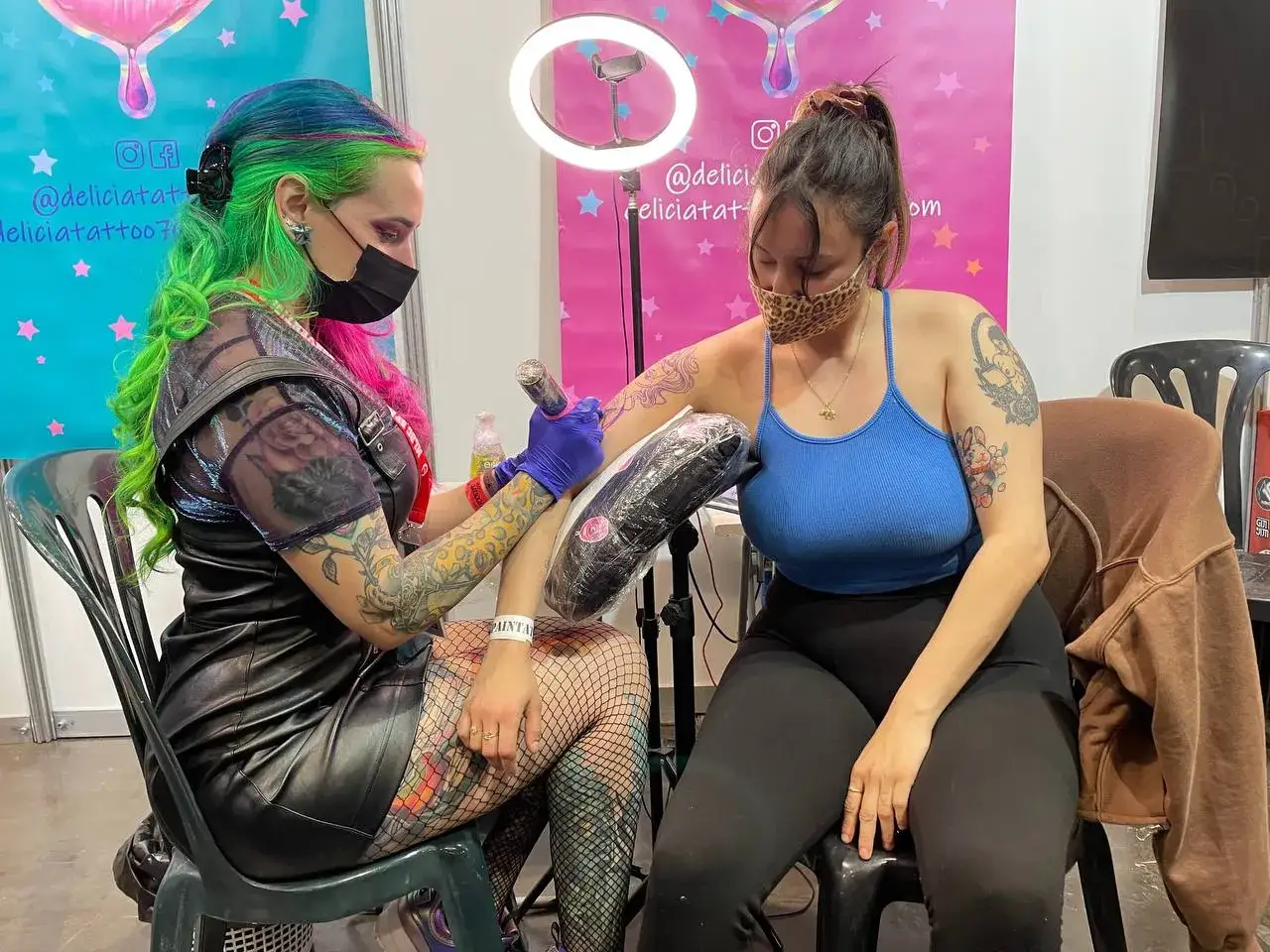 Artista con pelo verde y rosa tatuando brazo de clienta en la convenci&oacute;n tatuajes Valencia.