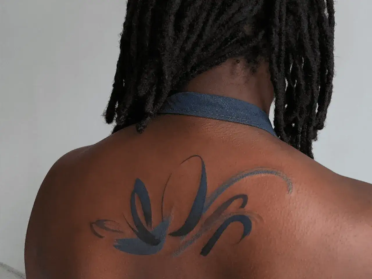 Tatuajes color piel con trazos oscuros y fluidos en la espalda de una persona con rastas.