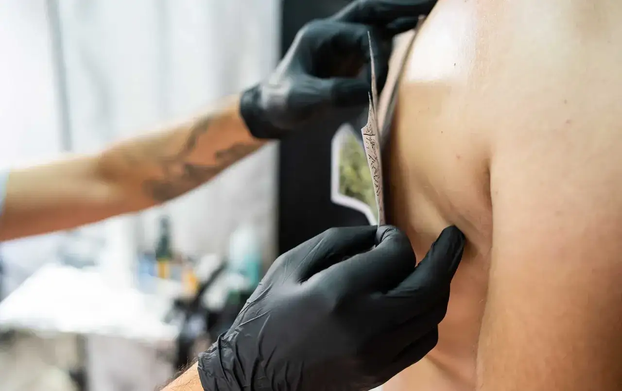 Man se prepara para hacerse un tatuaje, el artista coloca la plantilla en su hombro.