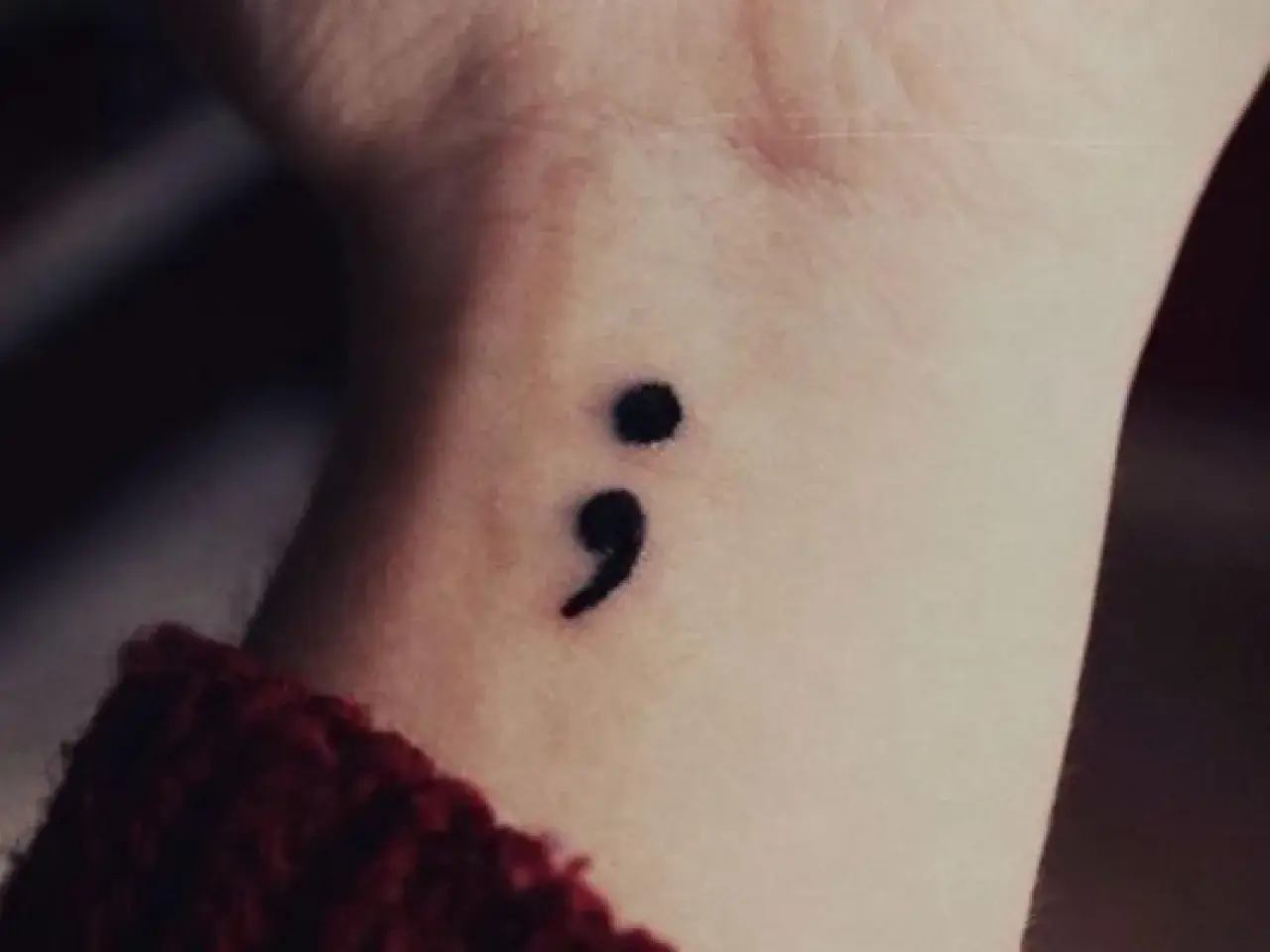 Un delicado tatuaje de punto y coma en la muñeca, símbolo de esperanza y resiliencia.