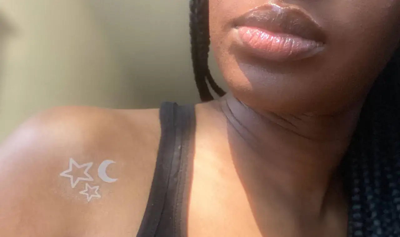 Un delicado tatuaje de tinta blanca con estrellas y luna sobre piel negra.