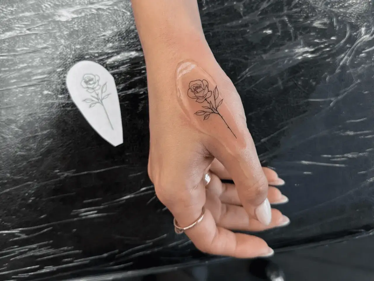 Una mano con un tatuaje de rosa en proceso. El dise&ntilde;o, similar a una plantilla de amoxicilina, se est&aacute; aplicando.