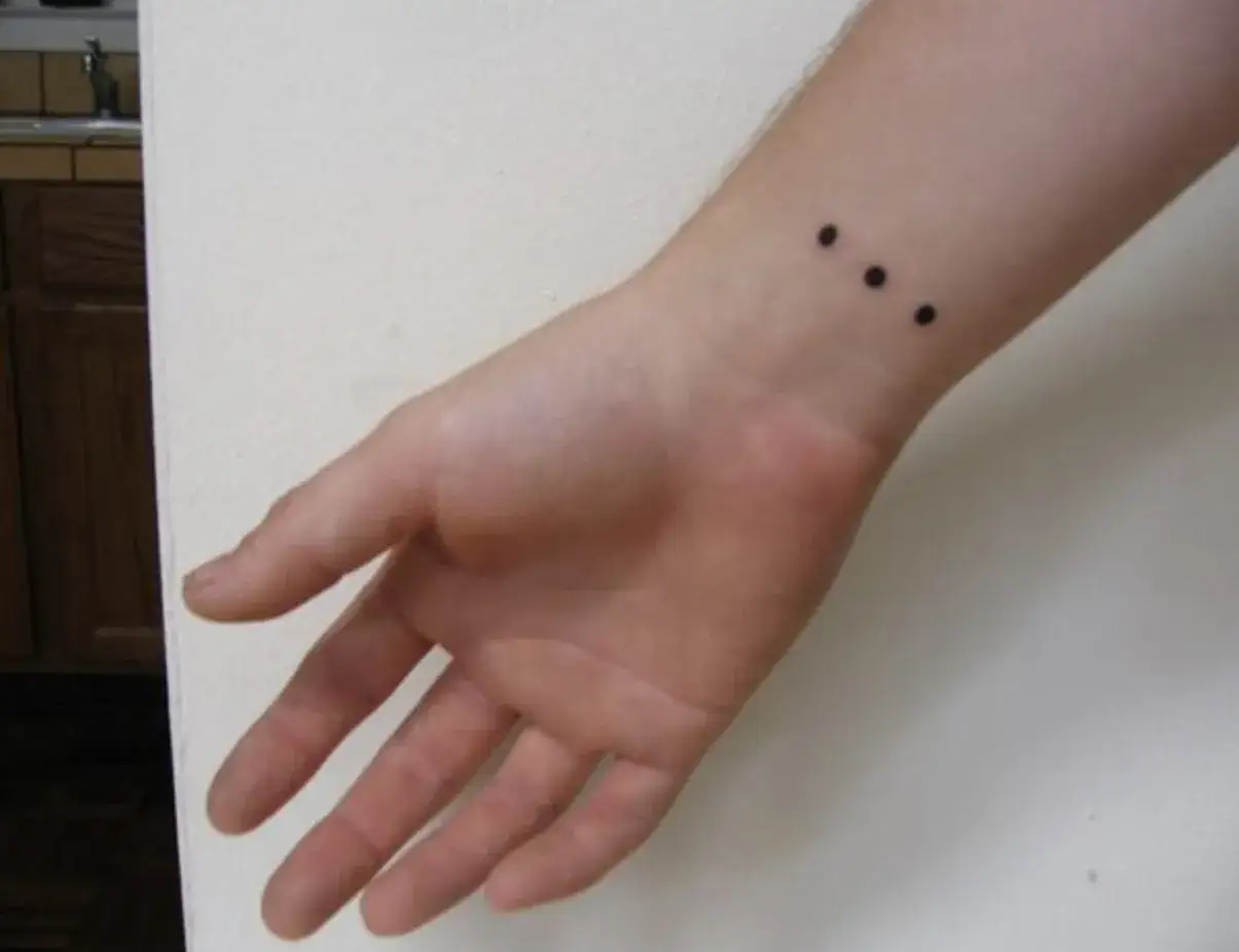 Mu&ntilde;eca con un discreto tatuaje de tres puntos negros alineados.