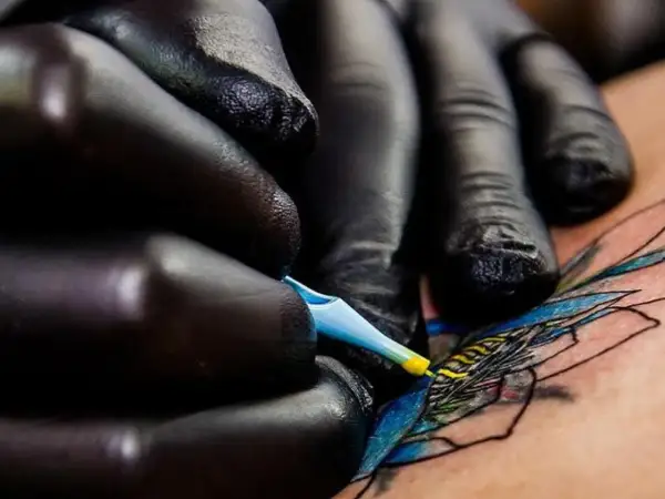 Manos enguantadas crean arte en piel, un detalle de los mejores tatuadores de España.