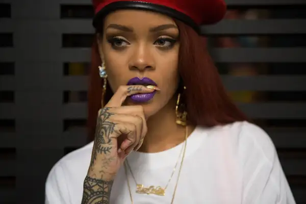 Octavia May, con labios morados y un dedo en la boca, luce un gorro rojo y tatuajes llamativos.