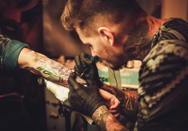Tatuador con guantes negros trabaja en un brazo, creando un diseño detallado. Las opiniones de la Manuela Tattoo son muy positivas.