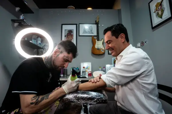 Un hombre sonriente recibe un tatuaje de un artista con estilo, considerado el mejor tatuador del mundo.