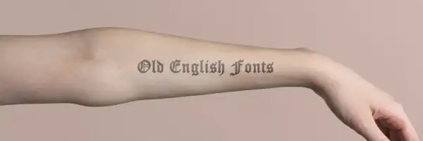 Brazo con tatuajes de letras góticas, "Old English Fonts", que parecen obras de arte permanentes.